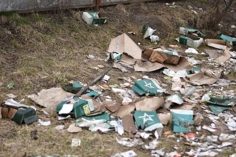 The image depicts a large pile of mixed waste materials scattered on a flat surface, likely outdoors or in a waste collection area. Visible among the debris are various empty plastic bottles, some wit